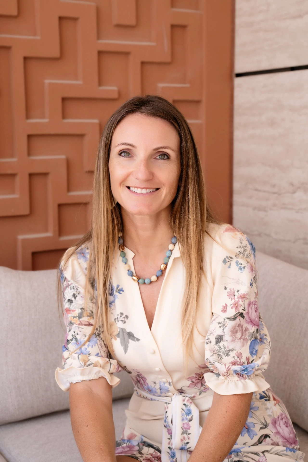 Andrea Mathis smiling in a floral dress in front of a warm terracotta lattice wall